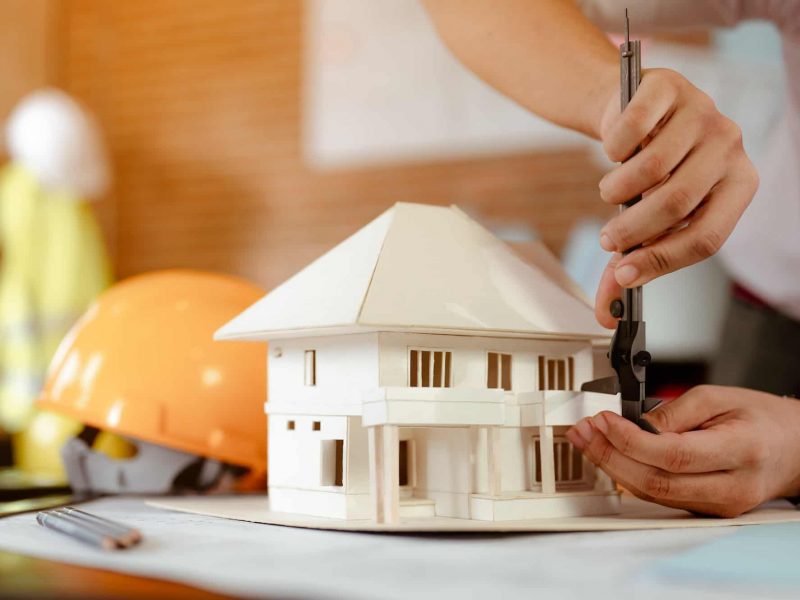 close-up-of-male-architect-hands-measuring-and-making-model-house-on-the-desk-at-sunset-.jpg